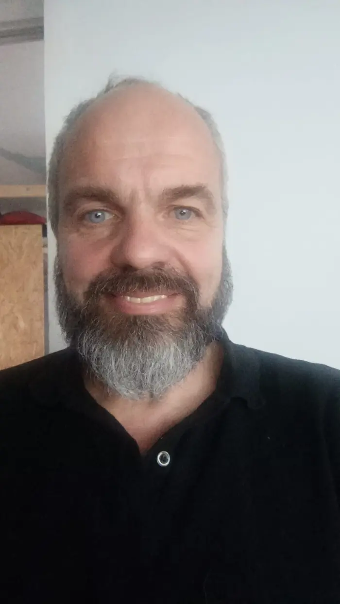Porträtfoto von Matthias Emberger: ein lächelnder Mann mit grauem Vollbart und schwarzem Hemd.